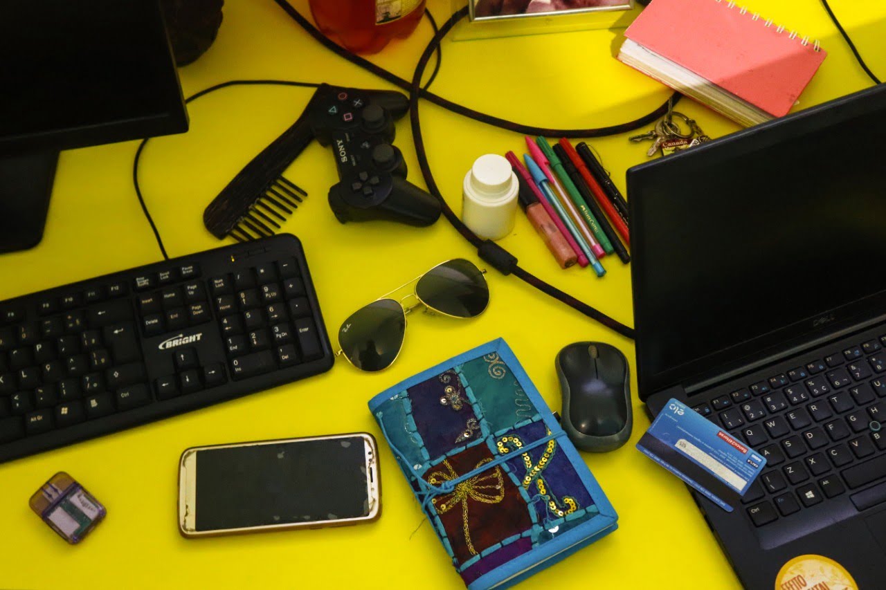 Computador, c elular e objetos pessoais sobre uma mesa amarela
