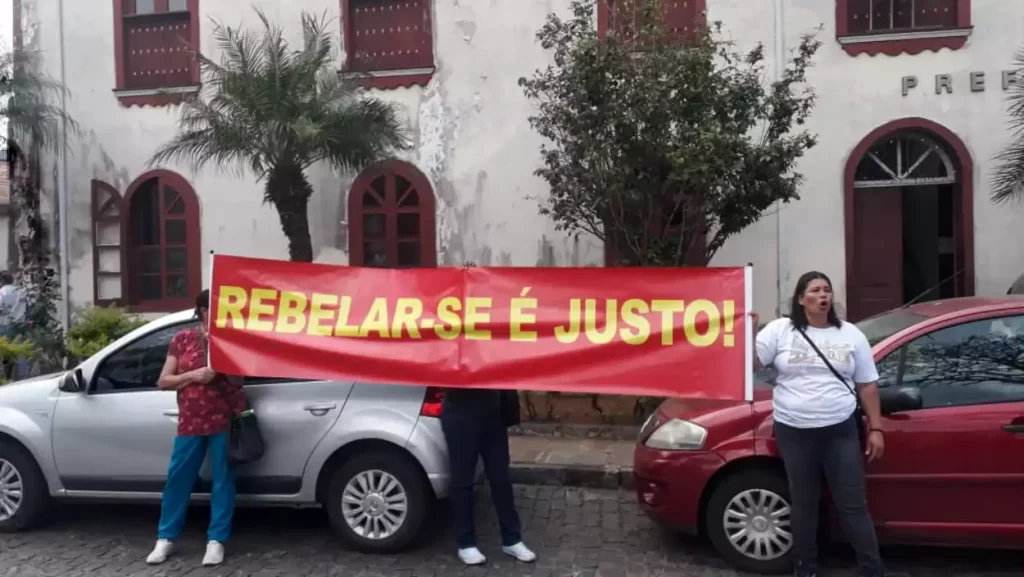 Manifestantes seguram faixa com os dizeres "Rebelar-se é Justo", á frente da Prefeitura de Ouro Preto, durante manifestação