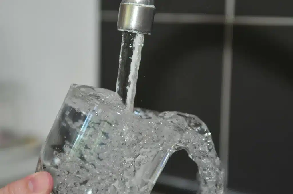Mão de uma pessoa segurando copo de água que transborda debaixo de uma torneira