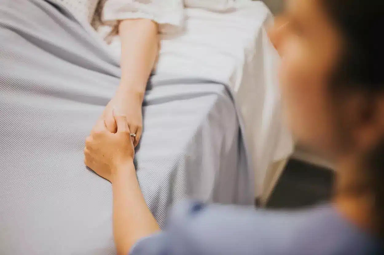 Acompanhante segurando a mão de uma mulher deitada em uma maca de hospital.