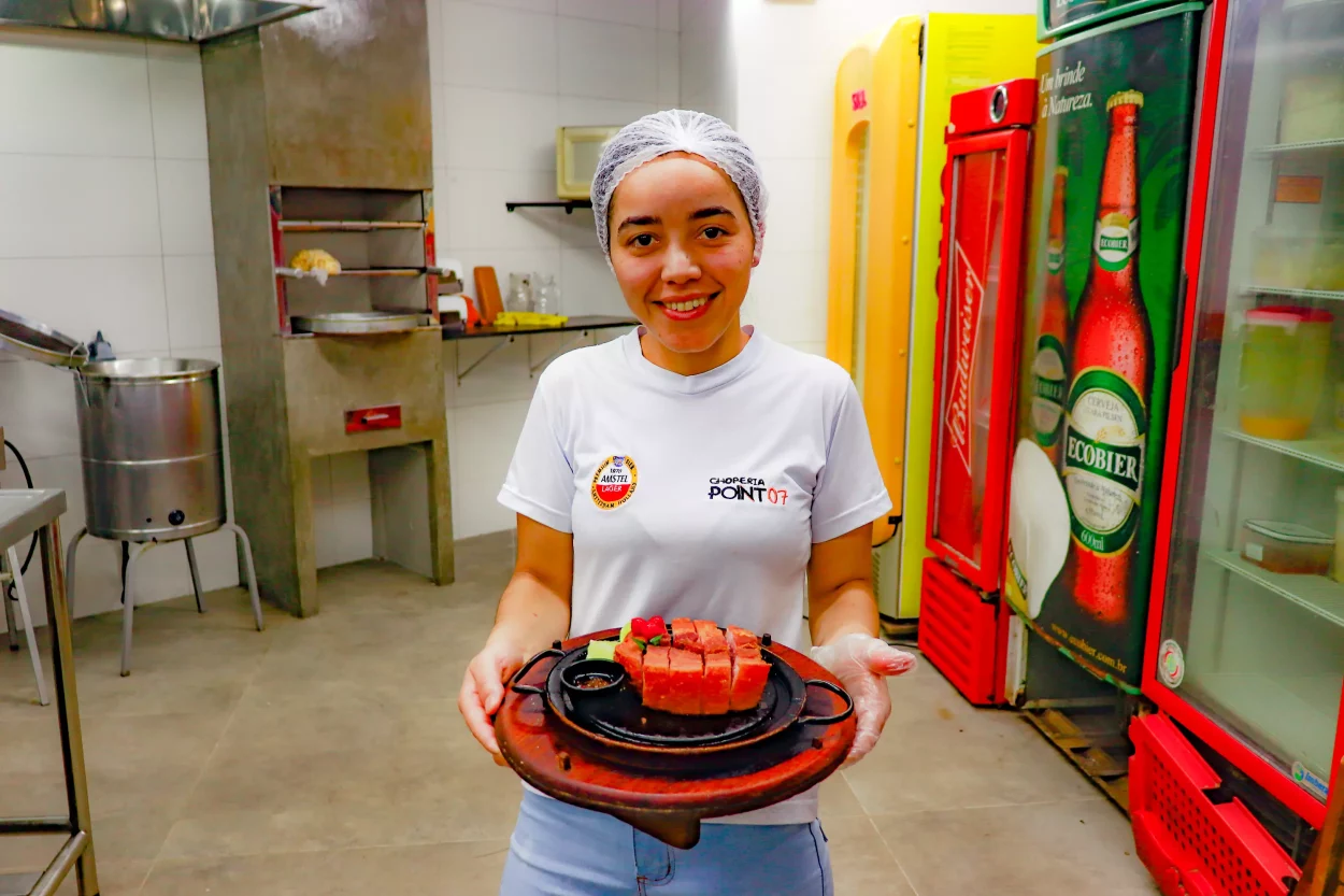 A chef Flaviana segura o tira-gosto na mão e sorri para a câmera