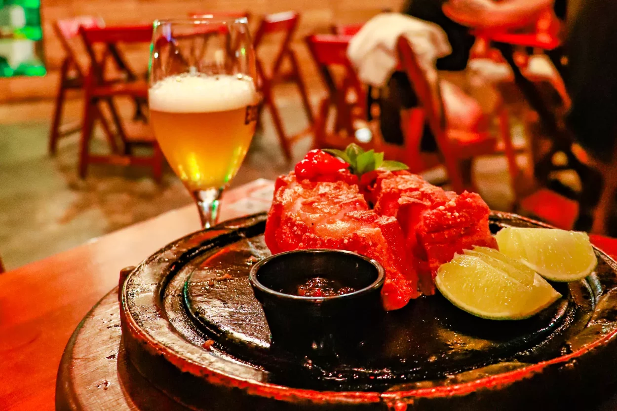 Em detalhe observamos o prato de pedra com o toucinho de rolo empanado com a geléia de pimenta e um limão partido, ao fundo tem um copo de cerveja