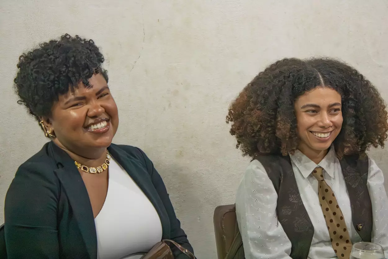 Laís Amaral e Gessimara Barbosa, duas psicólogas negras sorrindo, sentadas