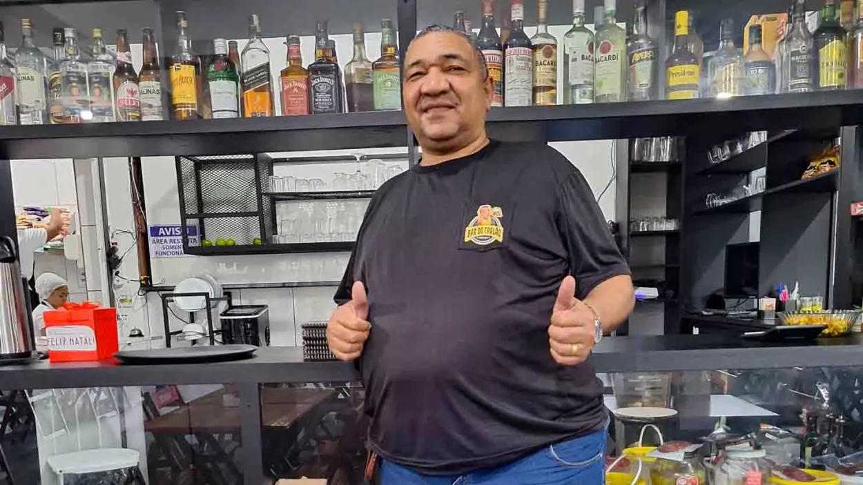 Carlão posa em frente seu bar com os dedos fazendo um joinha