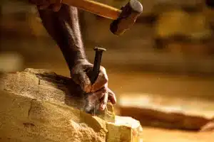 a imagem mostra uma pessoa quebrando pedra na escola de oficios tradicionais de mariana