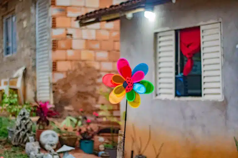 A imagem mostra um catavento colorido em frente uma casa construída na ocupção da Vila Serrinha, em Mariana