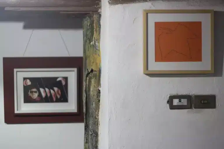A imagem mostra alguns quadros pendurados na parede da galeria porão